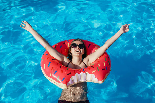 Beautiful young woman with pink donut circle have rest  in blue swimming pool