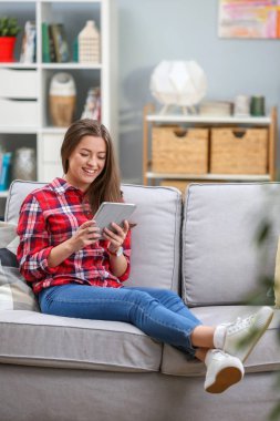 Bir koltukta evde dinlenirken dijital tablet kullanma çekici bir genç kadın portresi