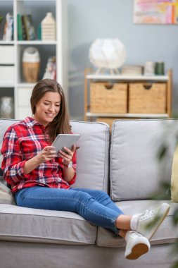Bir koltukta evde dinlenirken dijital tablet kullanma çekici bir genç kadın portresi