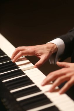 Piyano ellerinde. Piyanist piyano çalıyor. Siyah arka plan üzerine piyano tuşları