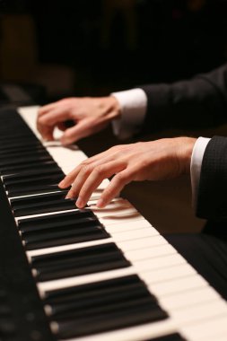Piyano ellerinde. Piyanist piyano çalıyor. Siyah arka plan üzerine piyano tuşları