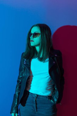 Pembe anf mavi neon ışıkları arka plan koyu gözlük deri ceket moda kız. 