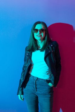 Pembe anf mavi neon ışıkları arka plan koyu gözlük deri ceket moda kız. 