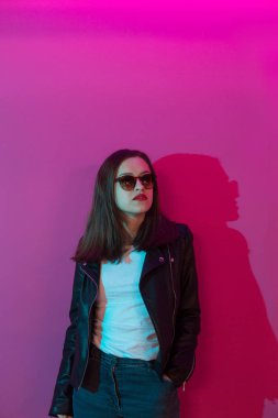 Pembe anf mavi neon ışıkları arka plan koyu gözlük deri ceket moda kız. 