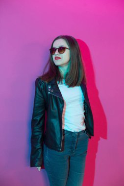 Pembe anf mavi neon ışıkları arka plan koyu gözlük deri ceket moda kız. 
