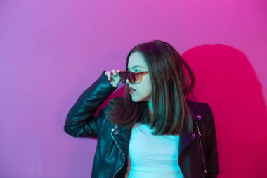 Pembe anf mavi neon ışıkları arka plan koyu gözlük deri ceket moda kız. 
