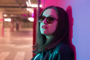 Pembe anf mavi neon ışıkları arka plan koyu gözlük deri ceket moda kız. 