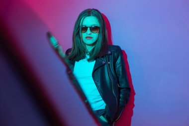 Pembe ve mavi neon ışıkları arka planda koyu gözlük deri ceket moda kız. 