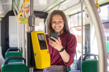 Kadın Kadın tramvayda toplu taşıma için akıllı telefon ile conctactless ödeme. Modern tramvayda sarı bilet makinesi