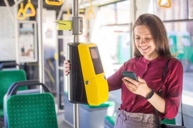 Kadın Kadın tramvayda toplu taşıma için akıllı telefon ile conctactless ödeme. Modern tramvayda sarı bilet makinesi