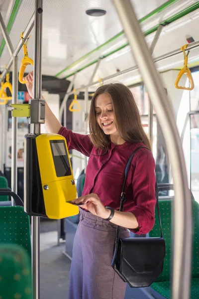 Kadın Kadın tramvayda toplu taşıma için akıllı telefon ile conctactless ödeme. Modern tramvayda sarı bilet makinesi