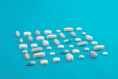 Çeşitli ilaç hapları, haplar ve kapsüller mavi arka planda.