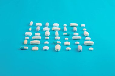 Çeşitli ilaç hapları, haplar ve kapsüller mavi arka planda.