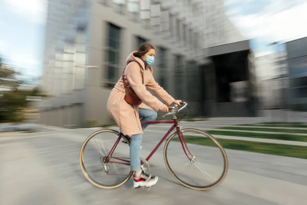 Young woman in face medical mask riding bicycle roadway motion blur