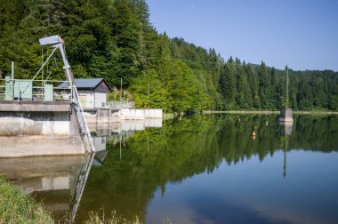 Bir baraj ve kontrol istasyonu yoğun bir ormanla çevrili bir su deposundaki su seviyelerini yönetir. Yapı, su ve sel kontrolünü güvence altına alıyor..