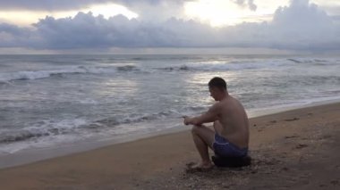 Gün batımında tropikal okyanus sahilde cep telefonu ile genç adam