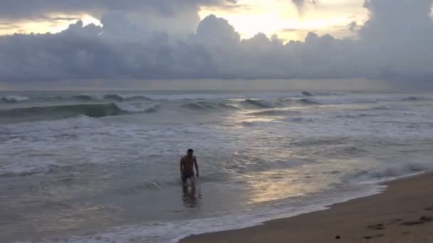 若い男は日没時にビーチで熱帯の海から出てくる — ストック動画
