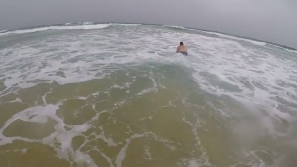 若い男は雨の中で海のサーフボードで泳ぐことを学ぶ — ストック動画