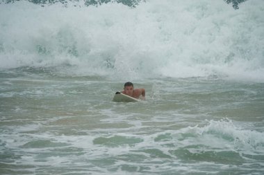 Genç adam okyanusta bir sörf tahtasında yüzer