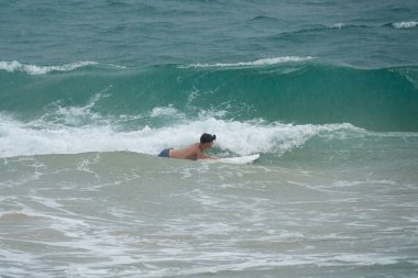 Genç adam okyanusta bir sörf tahtasında yüzer