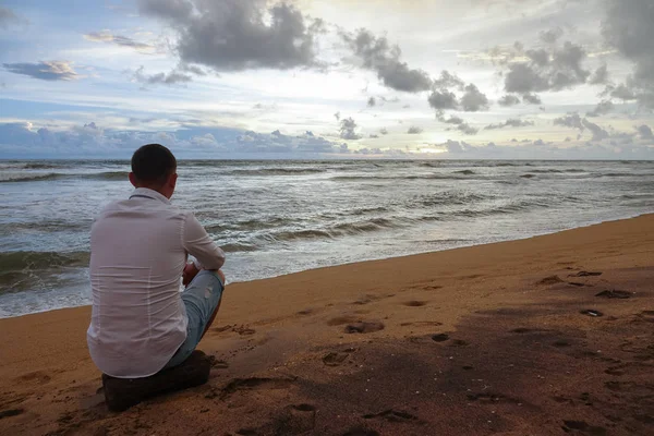 Un joven con una camisa blanca se encuentra con la puesta de sol en una playa tropical del océano Fotos de stock