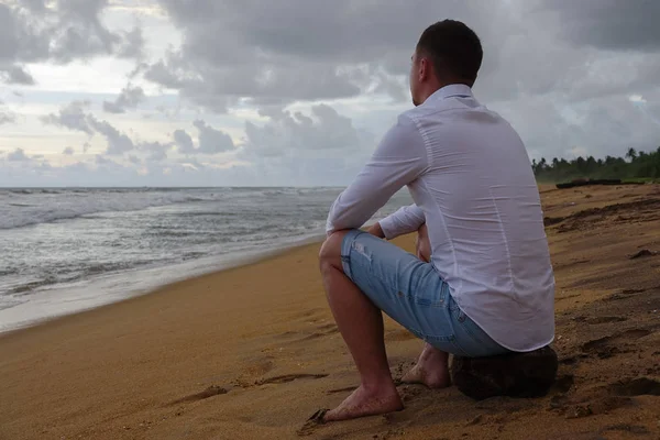 Un joven con una camisa blanca se encuentra con la puesta de sol en una playa tropical del océano Fotos de stock libres de derechos