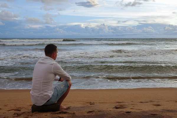 Un joven con una camisa blanca se encuentra con la puesta de sol en una playa tropical del océano Imágenes de stock libres de derechos