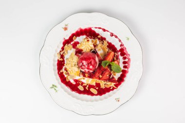 Bir kepçe dondurma, badem gevreği ve nane yaprağı ile nefis çilekli turta dilimi tabakta servis edilir..