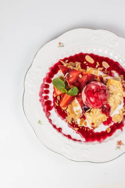 Bir kepçe dondurma, badem gevreği ve nane yaprağı ile nefis çilekli turta dilimi tabakta servis edilir..