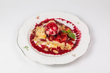 Dondurma kepçeli zarif çilekli tart, badem gevreği ve beyaz tabakta nane yaprakları, menüler ya da reklamlar için mükemmel..