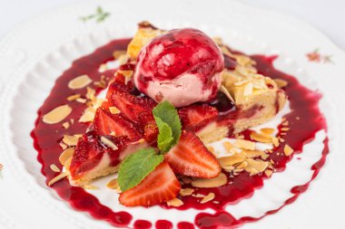 Bir dilim çilekli turtayı yakın plan beyaz arka planda bir kepçe dondurma ve badem gevreğiyle servis et..