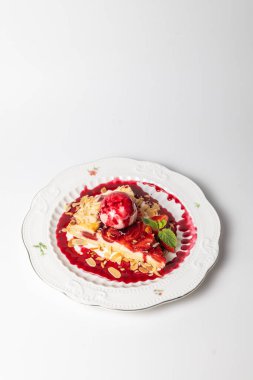 Bir dilim çilekli turtayı yakın plan beyaz arka planda bir kepçe dondurma ve badem gevreğiyle servis et..