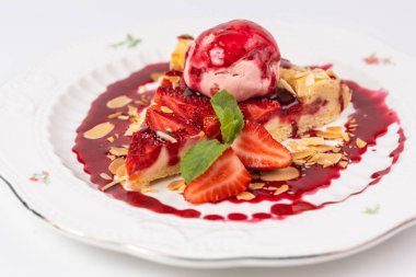 Bir dilim çilekli turtayı yakın plan beyaz arka planda bir kepçe dondurma ve badem gevreğiyle servis et..