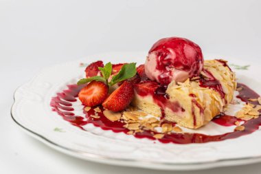 Bir kepçe dondurma, badem gevreği ve nane yaprağıyla servis edilen çilekli turta dilimini kapat..