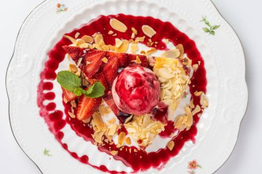 Çilekli turta dilimini kapat ve bir kepçe dondurma, badem gevreği ve nane yaprağıyla servis et..