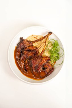 Kahverengi soslu, garnitürlü ve otlu ızgara kuzu pirzolası, beyaz arka planda sunuluyor, restoran menüsü tasarımı için mükemmel..