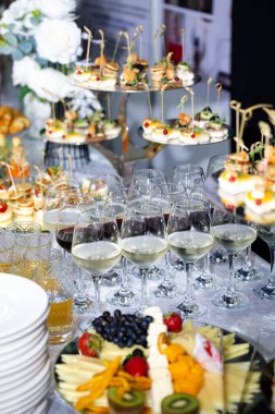 Kırmızı ve beyaz şarap bardakları, tepsilerde çeşitli kanepeler ve meyve ve peynir tabağı olan şenlikli bir büfe masasının yakın çekimi. Kutlama, düğün ya da kurumsal etkinlik için şık yemek organizasyonu..