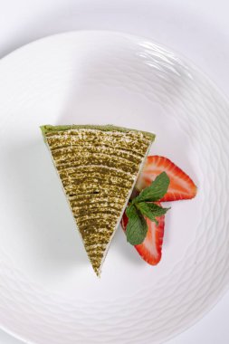 Çilekli ıspanaklı cheesecake dilimi ve beyaz arka planda nane şekeri.