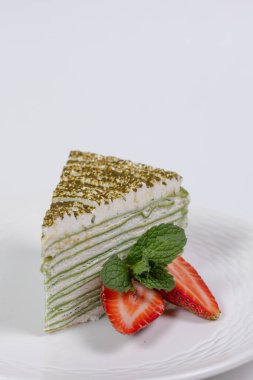 Beyaz arka planda çilekli ıspanaklı cheesecake dilimi ve nane şekeri.