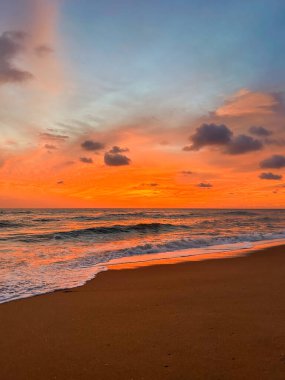 Vibrant sunset over the sea. Orange sky, turquoise waves, and sandy shore create a romantic atmosphere.