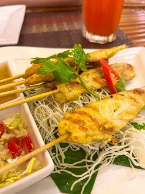 Grilled chicken skewers on bamboo sticks with sauce and herbs. Served on banana leaf and rice noodles.