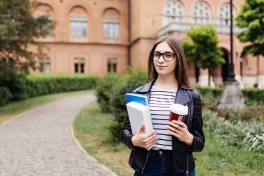Mutlu öğrenci kızla Üniversitesi arka plan, sırt çantası. Çalışma kitapları ve take away kahve dinlenme kampüsünde öğle yemeği molası sırasında sahip olan kadın.