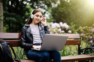 Gülümseyen öğrenci müzik dinleme ve dizüstü okul Park holding bankta oturmuş