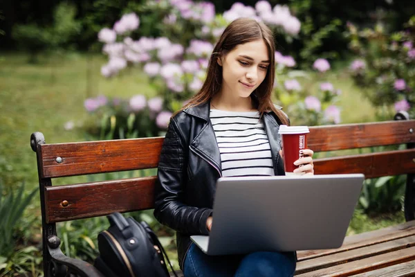 若い学生のラップトップで飲むコーヒー カップのベンチに座って 夏の公園で読書 — ストック写真