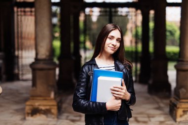 Mutlu genç kadın öğrenci kitap tutan ve açık havada yürüyüş sırt çantası ile