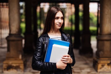 Mutlu genç kadın öğrenci kitap tutan ve açık havada yürüyüş sırt çantası ile