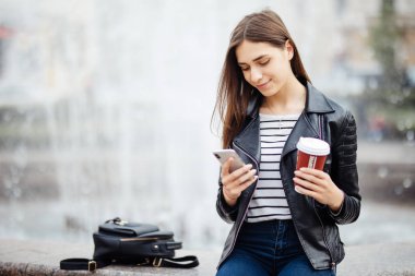 Çeşmenin ayakta ve onun smartphone açık havada kullanarak kadın.
