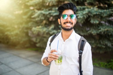 Güneş gözlüklü Genç Hintli adam portresi sokaklarda açık havada yaz içki mojito içmek