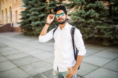 Güneş gözlüğü ve sırt çantası bir kentsel sokak genç yakışıklı Hintli adam portresi