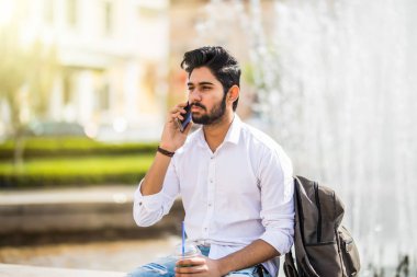 Çeşme oturan ve sokakta telefonda konuşurken yakışıklı genç Hintli adam